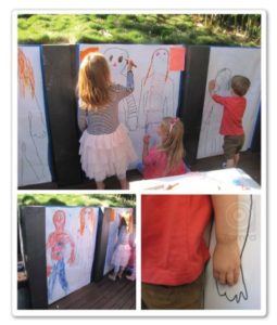 2 kids standing drawing onto a large sheet of paper with a superhero frame