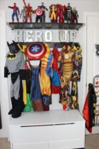 6 different superhero outfits hanging up with superhero figures above them on a shelf