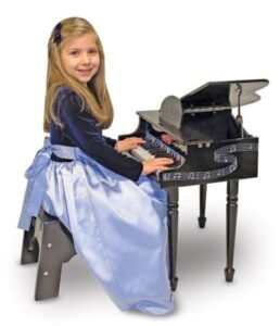 a kid girl sitting on a stool in a dress playing a kid piano
