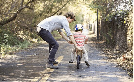 kid riding balance bike with dad pushing behind