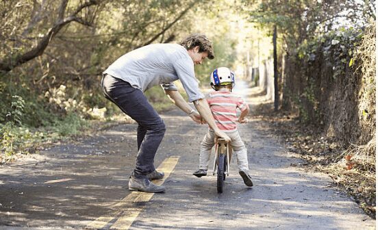 kid riding balance bike with dad pushing behind