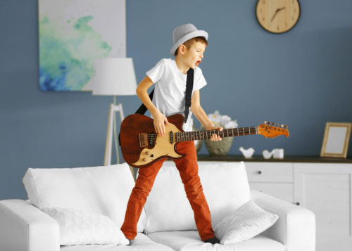 Little boy playing guitar ans singing on a sofa at home