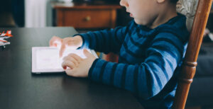 this is an image of a boy sitting at a table playing with a tablet