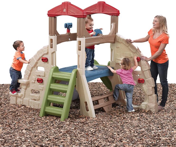 three toddlers with an adult play on a outdoor climbing toy in tan, red ang green colors.