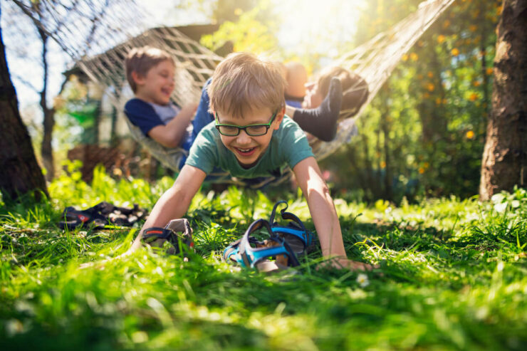 an image of a smiling boy playing in the grassy lawn with his companion in a hammock