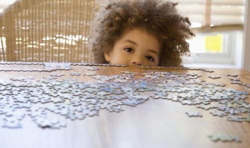 child completing a puzzle on the table with a lot of puzzle pieces