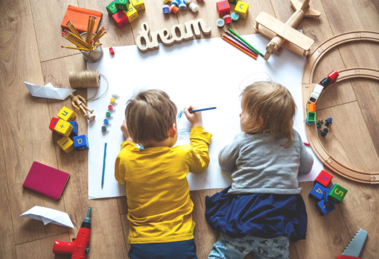 This is an image of kids on the floor playing and drawing surrounded by toys