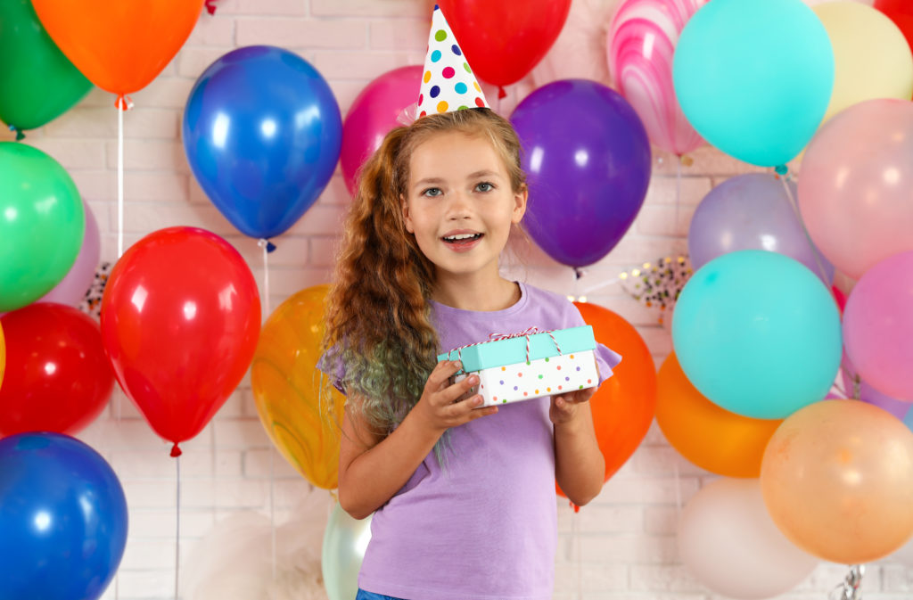 this is an image of a tween girl holding a gift beside some balloons