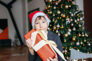 this is an image of a boy holding a gift beside a christmas tree