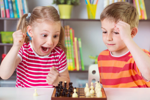 Two cute children playing chess at home