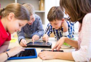 4 kids at a table playing with tablets and iPad 