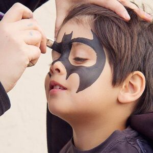 woman face painting a kid with a batman design 